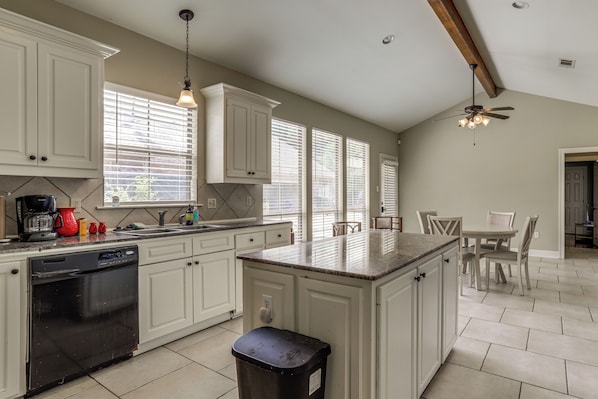 A kitchen with white cabinets, a dishwasher, a coffee maker, and a dining area with a table and chairs.