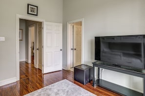 A room with hardwood flooring, a grey rug, a black entertainment unit with a TV, and white doors leading to other rooms.