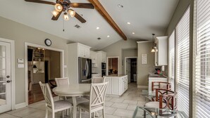 Una cocina moderna con muebles blancos, un comedor con mesa de vidrio y un ventilador de techo con iluminación.