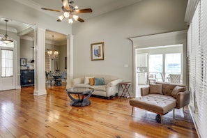 A spacious living room with hardwood flooring, a ceiling fan, a chandelier, and a dining area with a table and chairs.