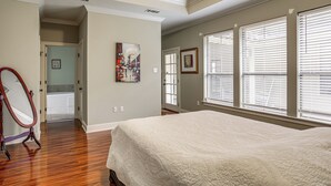 Un dormitorio con una cama grande, una puerta que da a un baño y una ventana con persianas.