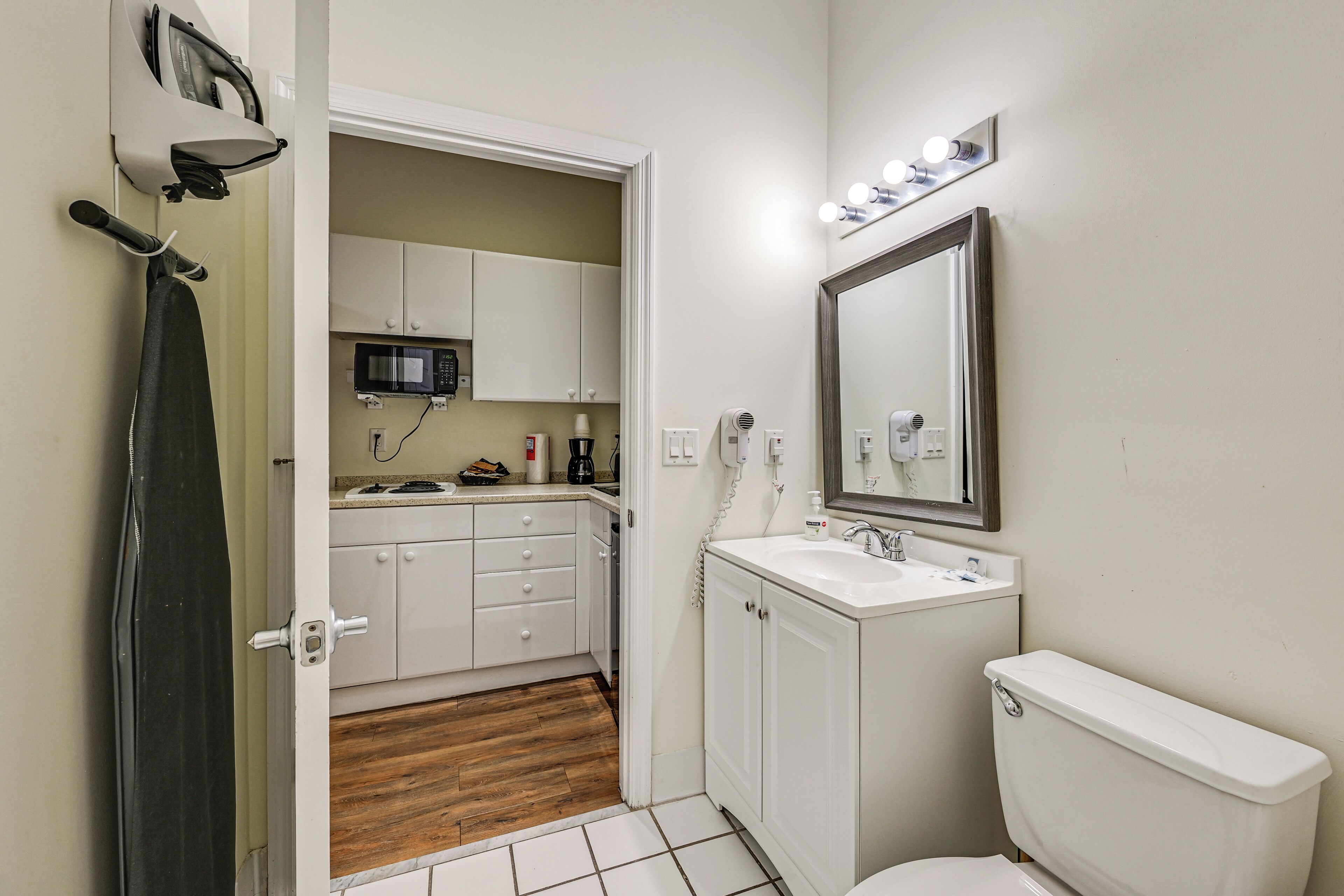 Un bagno compatto con toilette, lavandino e specchio. È presente una tenda da doccia, un forno a microonde e un armadietto nella zona cucina adiacente.