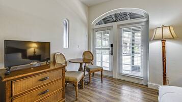 A room with a wooden dresser, a television, a dining table with chairs, and a lamp.