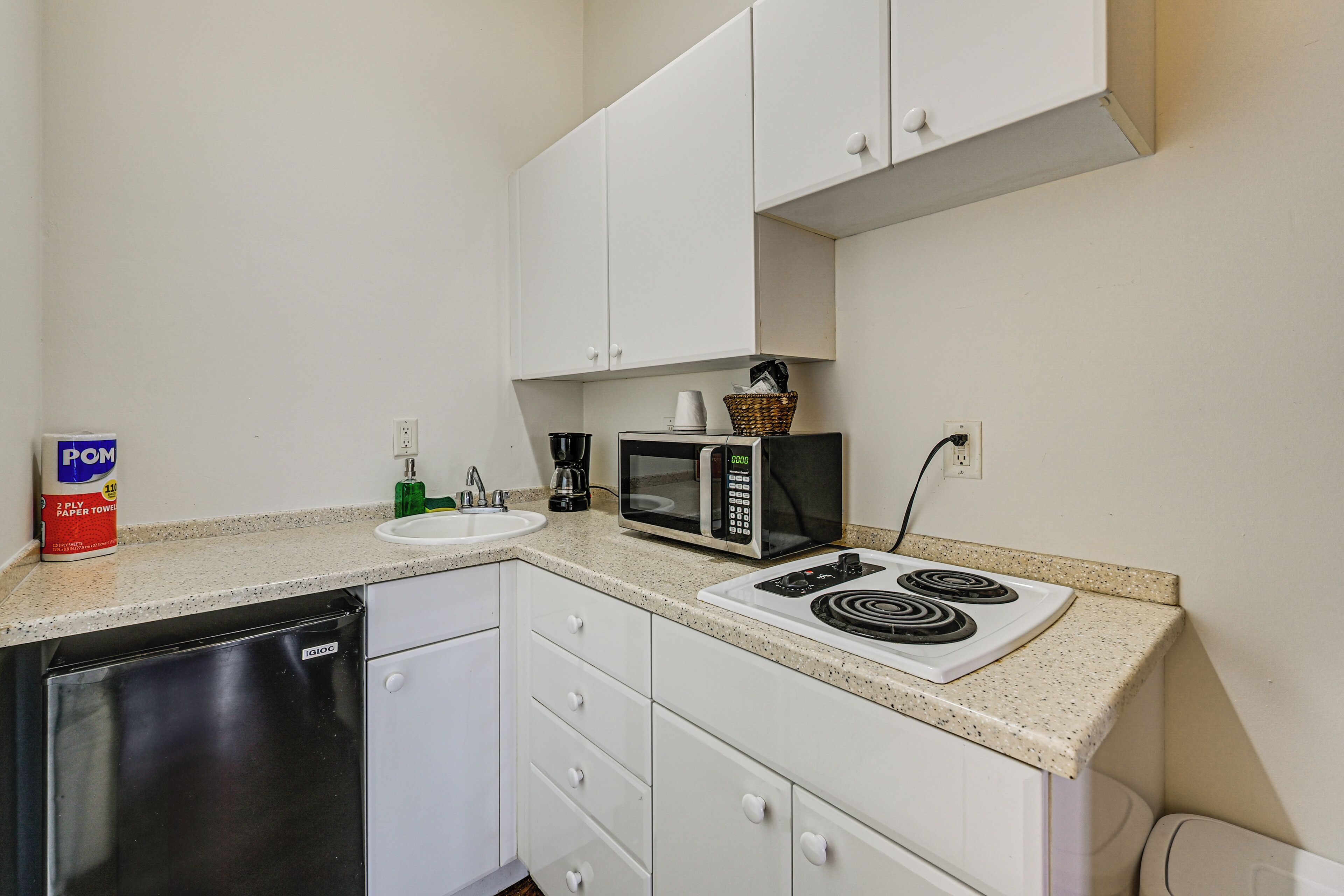 A compact kitchen with white cabinets, a microwave, a stove, a sink, and a dishwasher.
