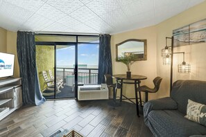 A modern hotel room with a balcony, a sofa, a dining table, and a TV.