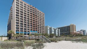 A high-rise hotel with multiple floors, a beach view, and a wooden staircase leading to the entrance.