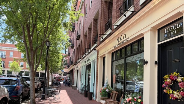 A brick building with a spa and aesthetics shop, outdoor seating, and parked cars along a tree-lined sidewalk. - 3-bedroom condo in Norton Commons (Prospect)