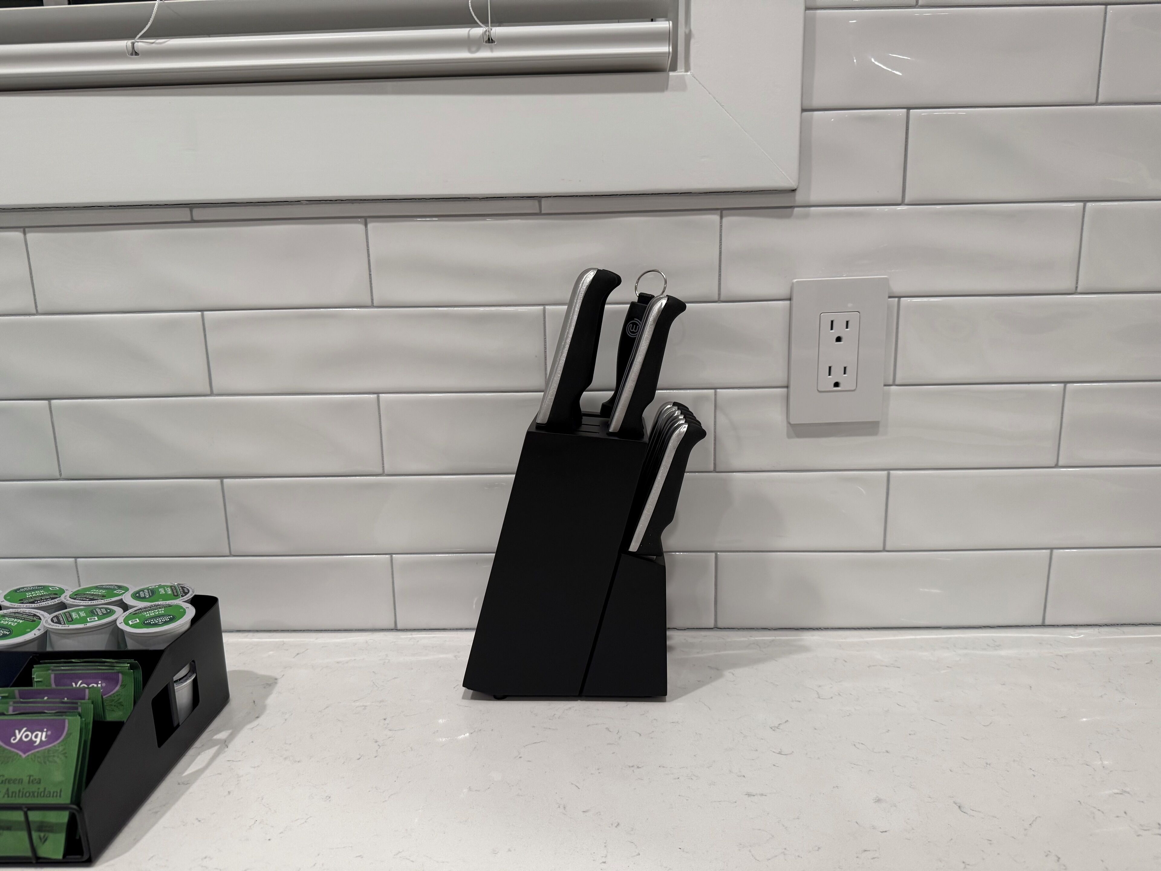 Une cuisine avec un dosseret de carrelage blanc, un bloc à couteaux noir et une boîte de thé vert antioxydant de la marque Yogi sur le comptoir.