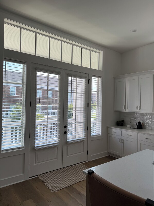 Una cocina con armarios blancos, una encimera y una ventana con persianas.
