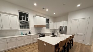 A modern kitchen with white cabinets, a central island with chairs, a stainless steel refrigerator, and a wooden floor. - 3-bedroom condo in Norton Commons (Prospect)