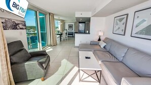 Un soggiorno moderno con un divano grigio, una poltrona in pelle nera e un tavolino da caffè bianco. Una grande finestra offre vista sul mare e c'è un balcone.
