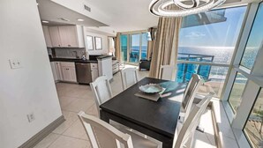 Una cucina moderna con mobili bianchi e una zona pranzo con tavolo nero e sedie bianche. Un'ampia finestra offre vista sull'oceano.