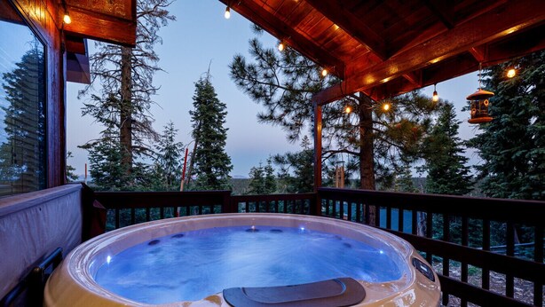 A hot tub on a wooden deck with a view of trees and a wooden structure overhead. - Strawberry Summit Cabin Retreat (Duck Creek Village)