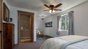 A bedroom with a bed, a ceiling fan, a rocking chair, and a window with curtains. - Strawberry Summit Cabin Retreat (Duck Creek Village)
