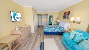 A bedroom with a bed, a blue sofa, a desk, a dresser, and a TV displaying 'BIG FISH Rentals'. - New Direct Oceanfront View Studio, Pools, Updated! (Myrtle Beach)