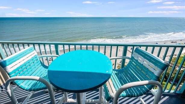 A balcony with a turquoise table and chairs overlooking a beach. - New Direct Oceanfront View Studio, Pools, Updated! (Myrtle Beach)