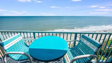 Ein Balkon mit einem türkisfarbenen Tisch und Stühlen mit Blick auf einen Strand.