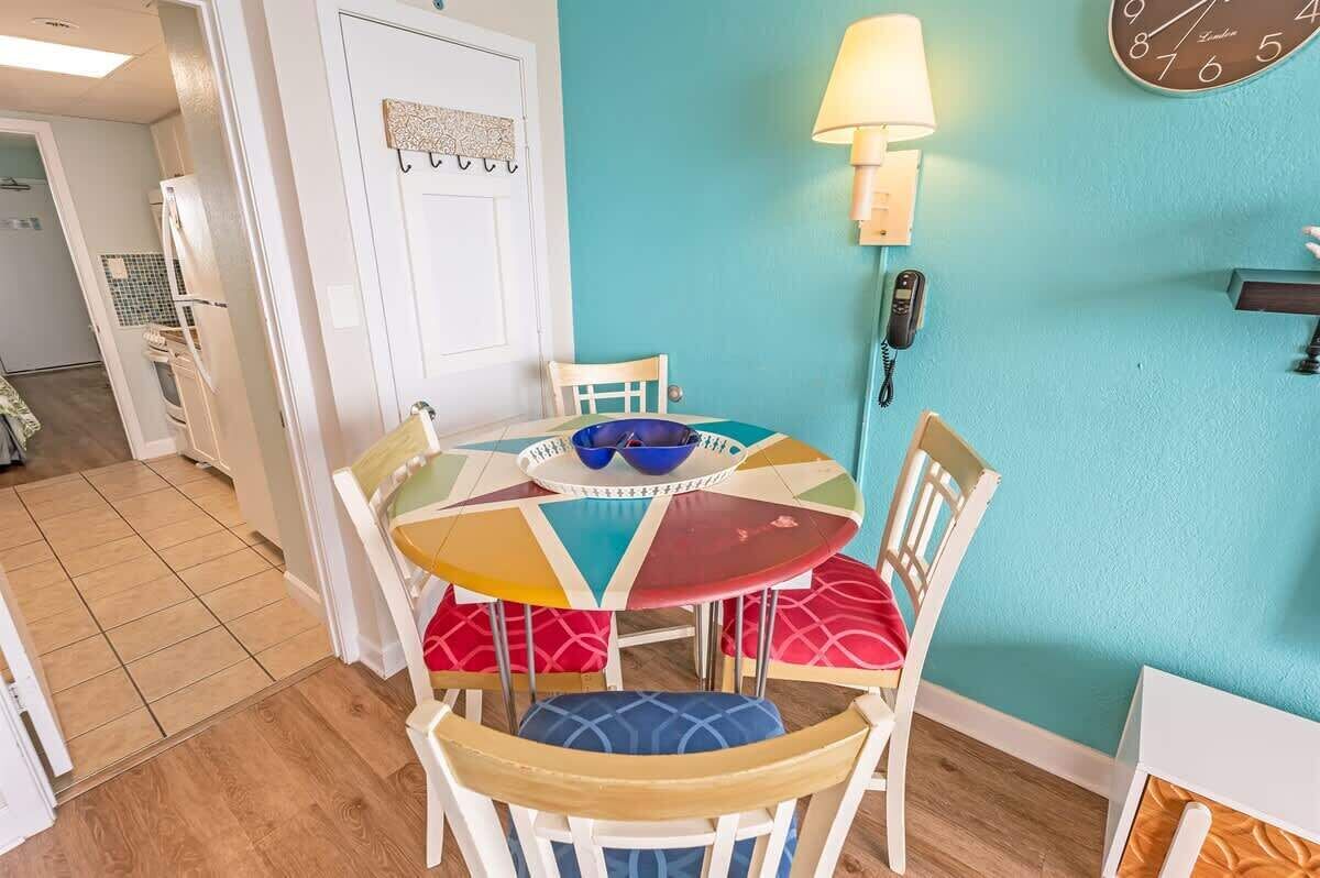 A dining area with a round table, colorful chairs, a wall clock, and a telephone.