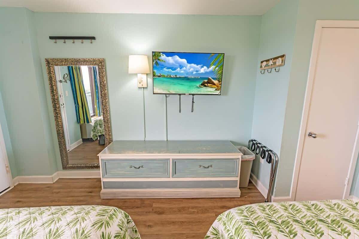 Una habitación con dos camas, televisión, espejo y lámpara.