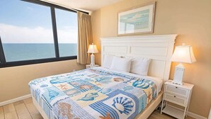 Une chambre à coucher avec un lit, deux tables de chevet, une fenêtre donnant sur la mer et un tableau accroché au mur.