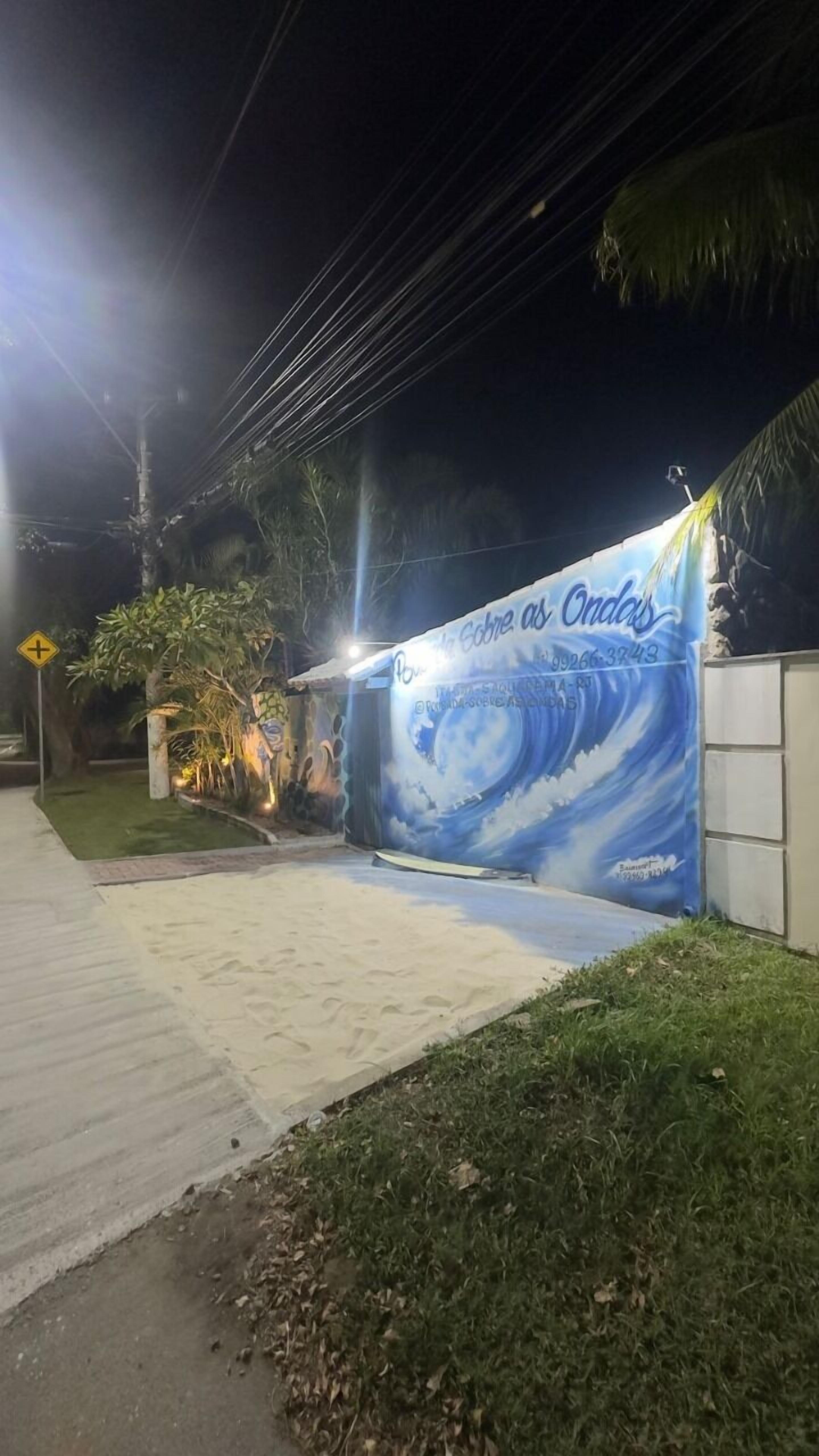 Une vue nocturne d’un bâtiment orné d’une grande fresque représentant une vague, avec l’inscription « Sobre as Ondas ».