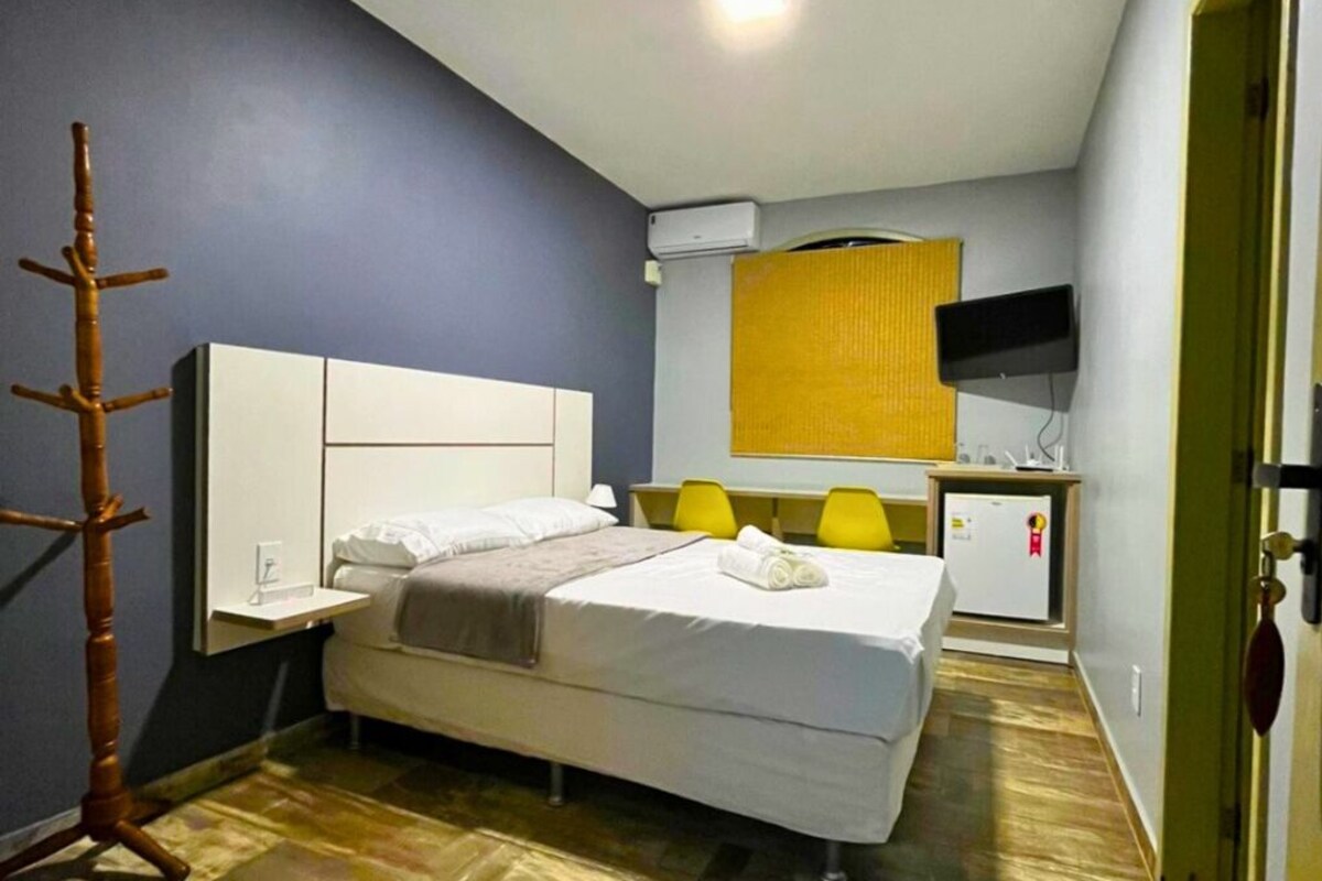 A hotel room with a bed, a desk with a chair, a TV, and a coat rack.