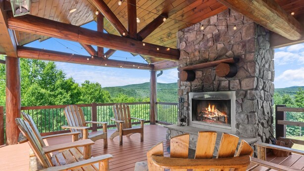 Una terraza de madera con sillas Adirondack, una chimenea de piedra y una vista panorámica.