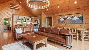 Amplia sala de estar con techo de madera, un sofá de cuero marrón grande, una mesa de centro de madera y un comedor con mesa y sillas de madera.