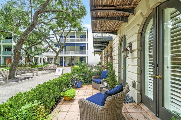 Un patio con mobiliario de mimbre, una planta en maceta y un edificio con balcones.