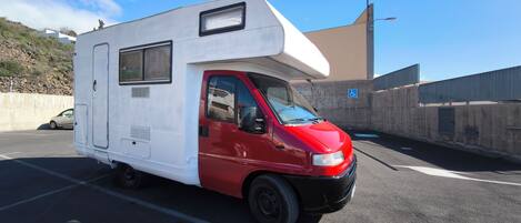 A white and red camper van parked on a road with a concrete barrier and a blue handicap sign in the background.