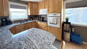 Une cuisine dotée de plans de travail en granit, de meubles en bois, d’un four à micro-ondes encastré, d’un four et d’une machine à café.