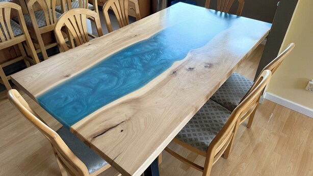 Une table de salle à manger en bois, ornée d’un motif unique en résine bleue, et entourée de chaises assorties.