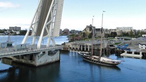 Eine Brücke mit einer weißen Struktur und einer Straße, eine Marina mit Booten sowie Gebäude im Hintergrund.