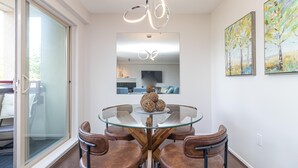 A modern dining area with a glass table, leather chairs, a unique ceiling light, and artwork on the walls. - Waterfront Condo and Walk to Town/Trails (Esquimalt)