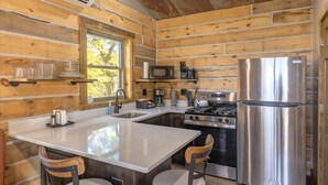 A compact kitchen with wooden walls, a central island, stainless steel appliances, and a window providing natural light.