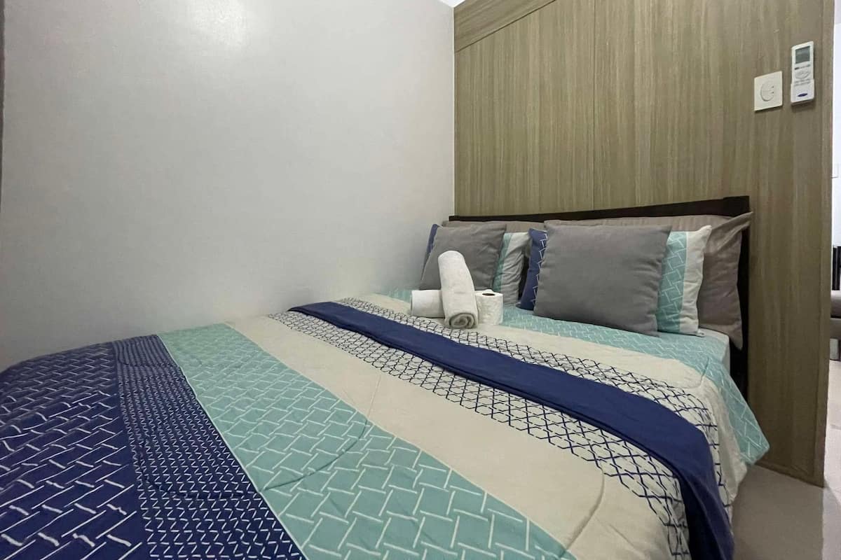 Een hotelkamer met een bed, een houten hoofdeinde en een thermostaat aan de muur.