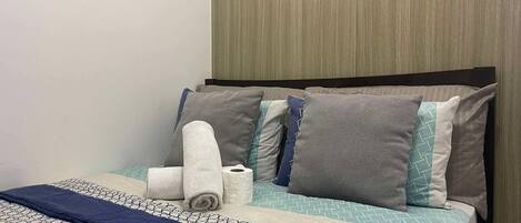 Een netjes opgemaakt bed met beddengoed met dessin, een donkerblauwe deken en meerdere kussens in verschillende tinten en patronen.