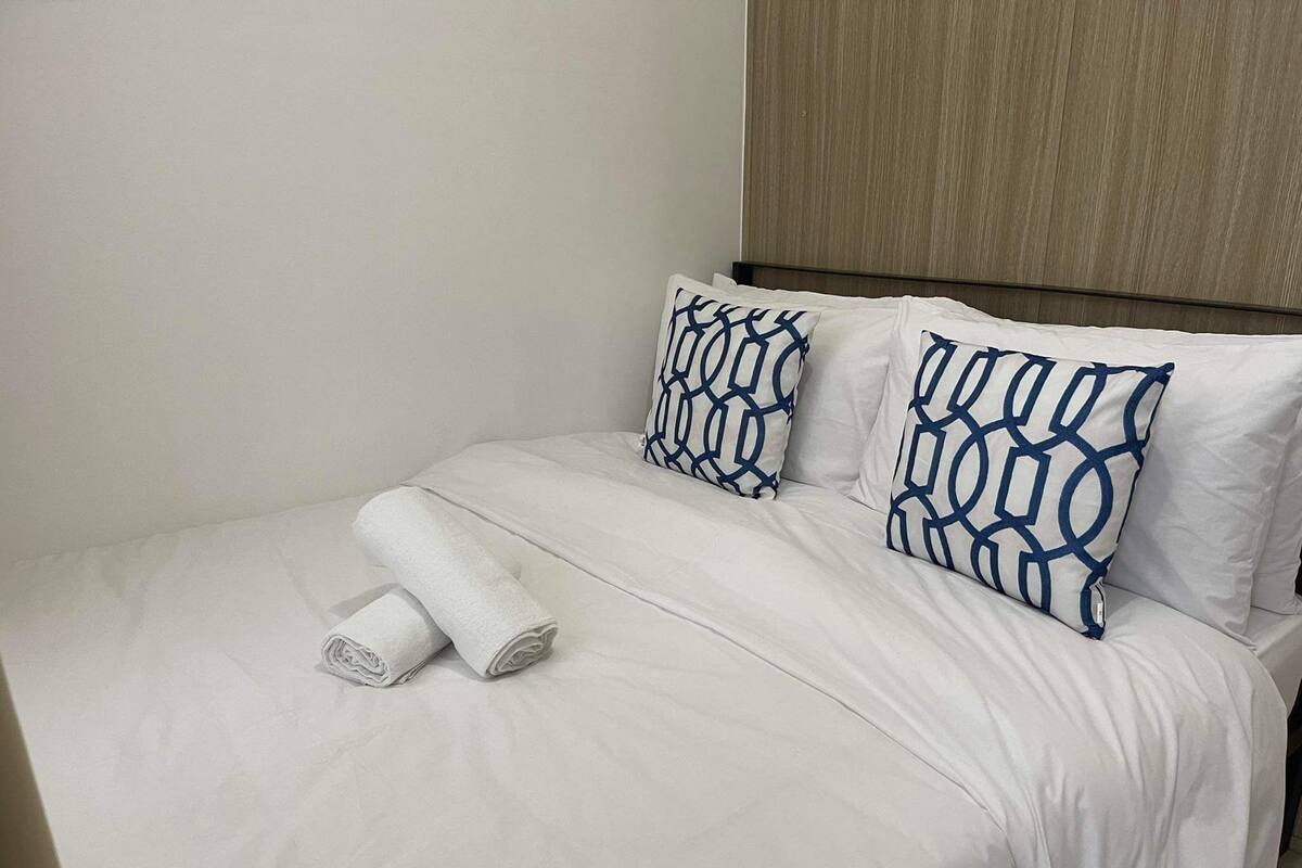 Een net opgemaakt bed met witte beddengoed en twee kussens met een geometrisch patroon.