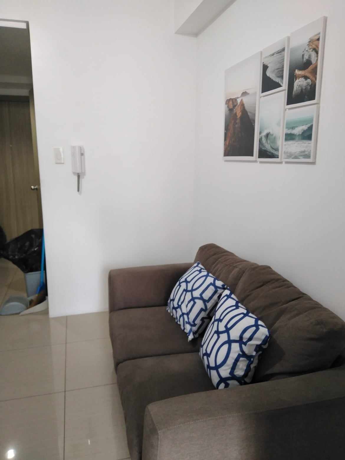 A living room with a brown sofa, two patterned cushions, and three framed pictures on the wall.