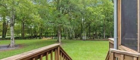 A wooden deck with a view of a grassy yard and trees.