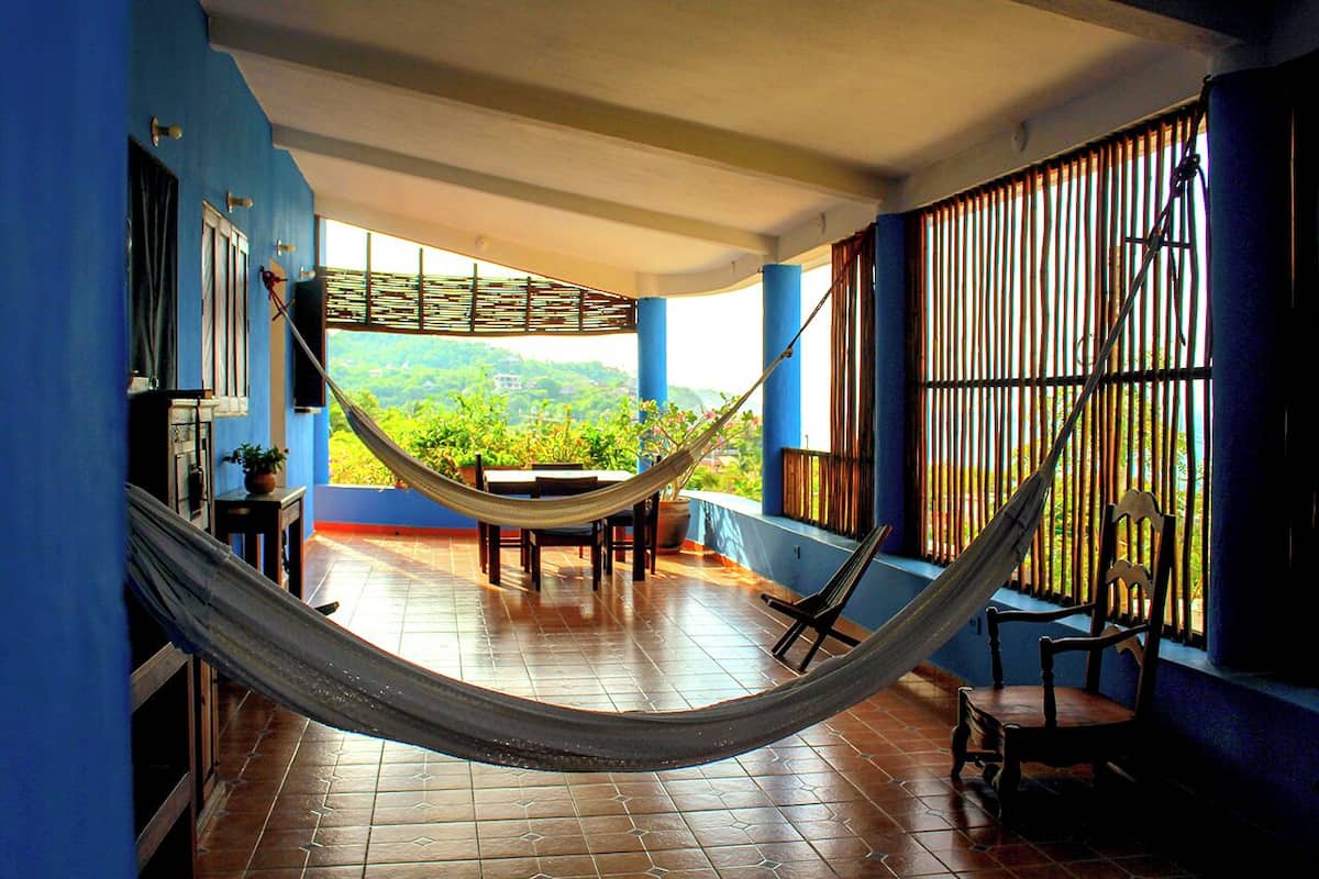 A hammock in a room with blue walls, a tiled floor, and a view of greenery outside.
