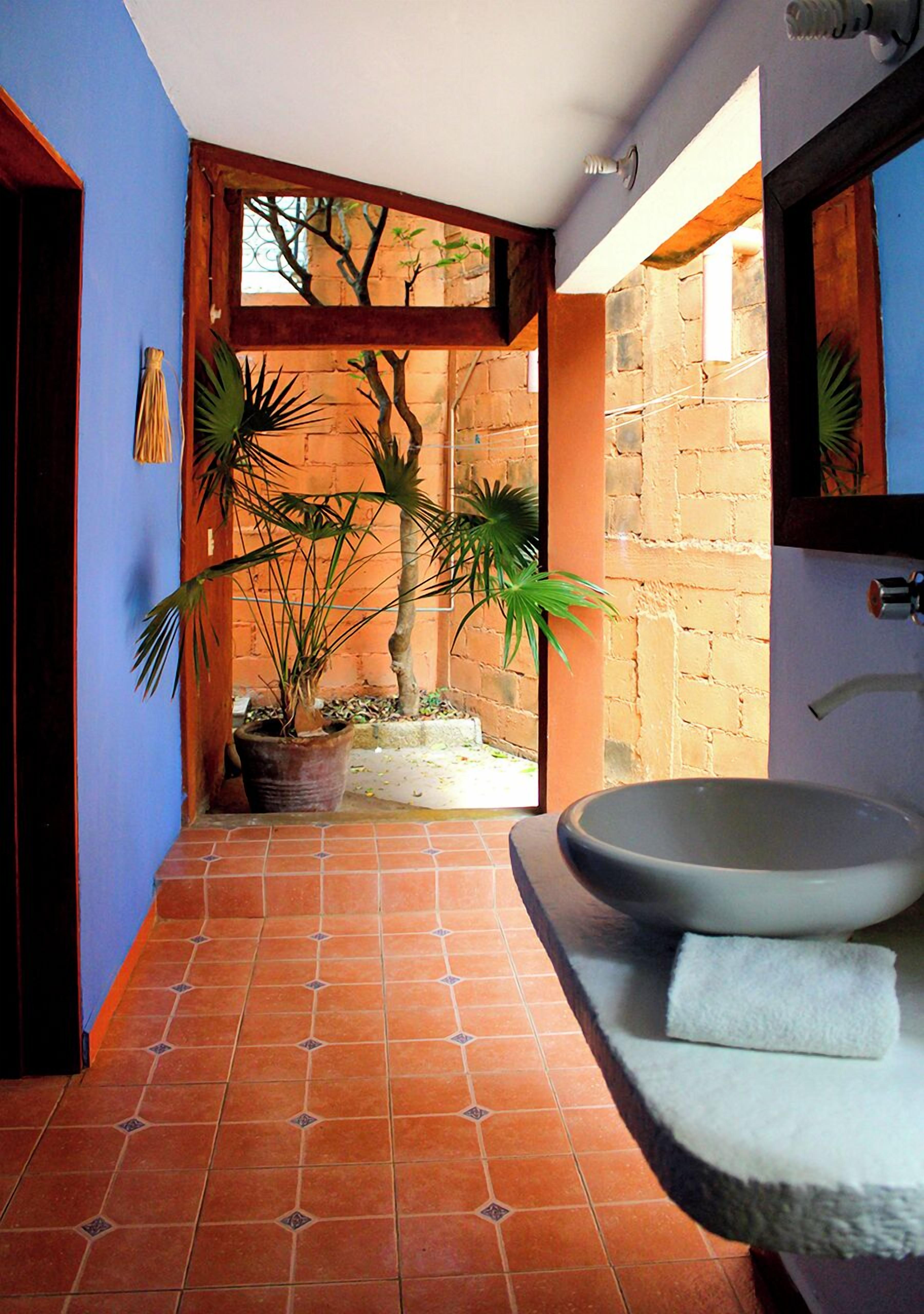 Un baño con un lavamanos de pedestal, un espejo y plantas en macetas.