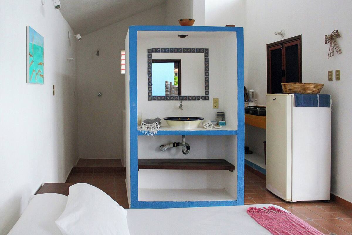 A compact hotel room with a bed, a small bathroom with a sink and mirror, and a kitchenette area.