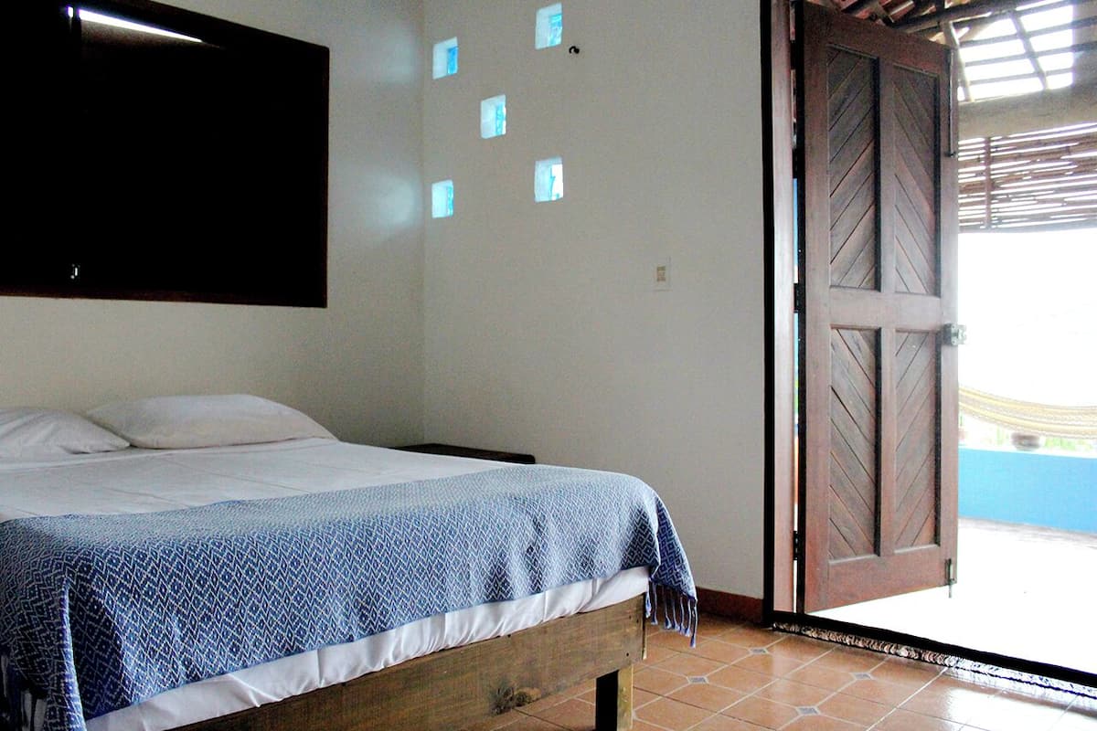 A bedroom with a bed, a wooden door, and a view of the outside.