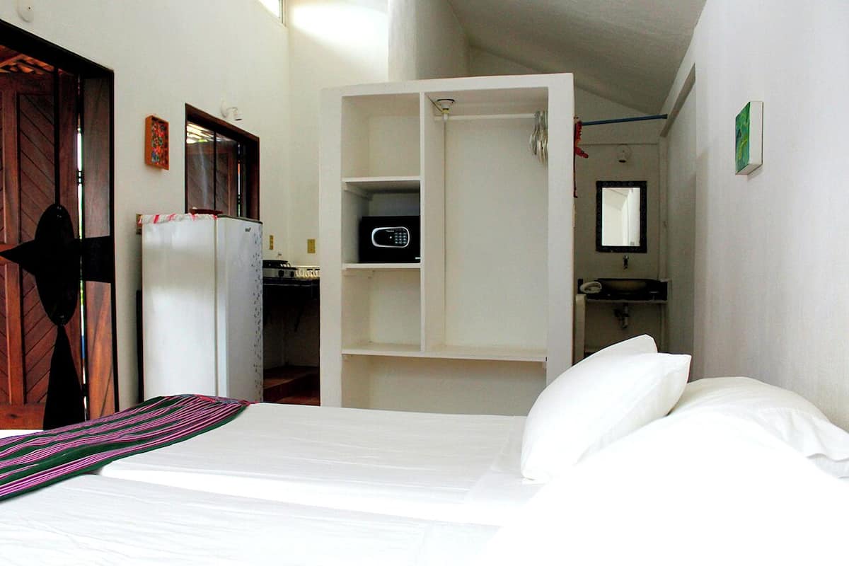 A hotel room with a bed, a wardrobe, a microwave, and a sink.