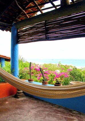 A hammock under a blue structure with a view of the ocean and pink flowers. - Casa Azul (Santa Maria Tonameca)