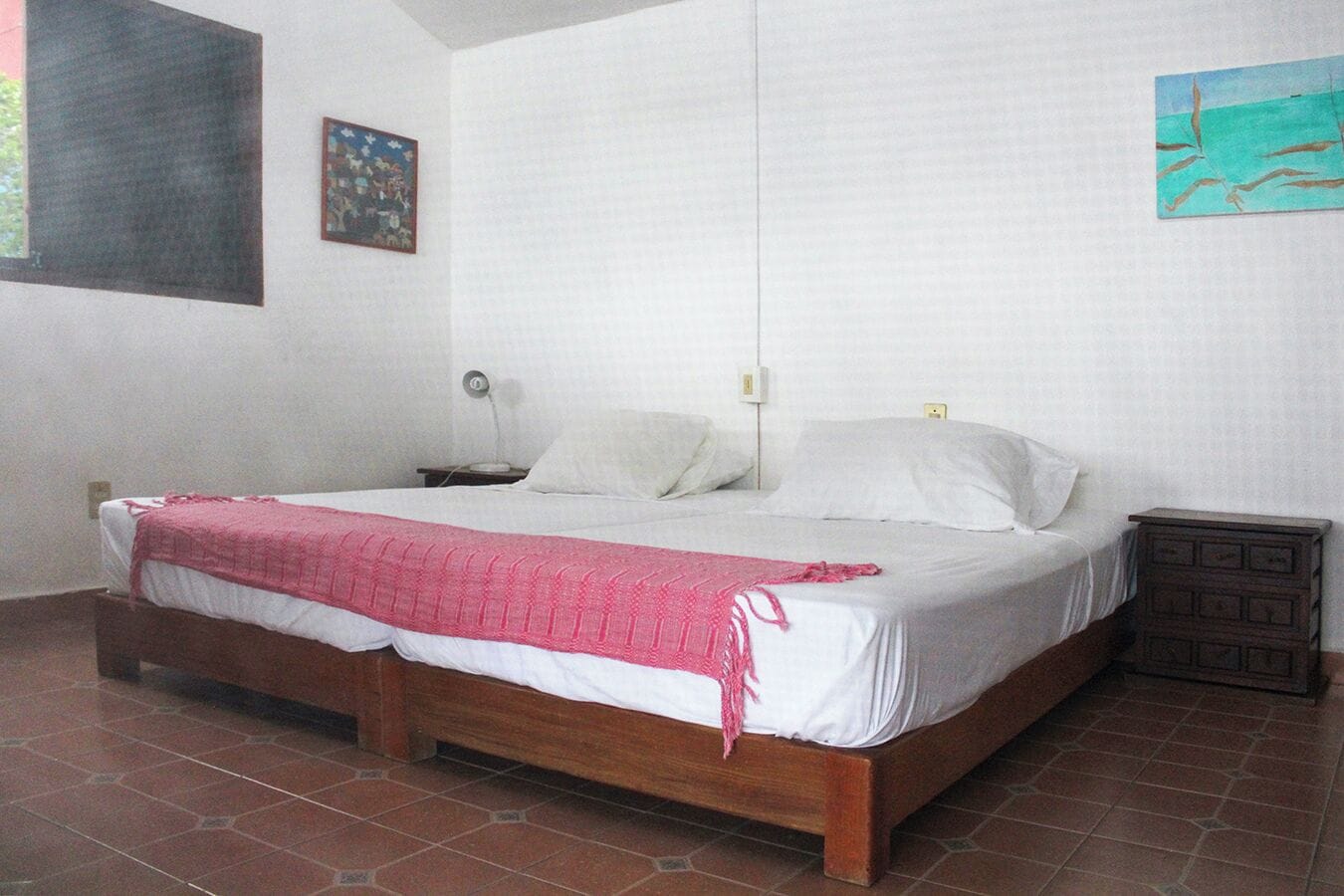 A single-bed room with a wooden frame, white bedding, and a red blanket.