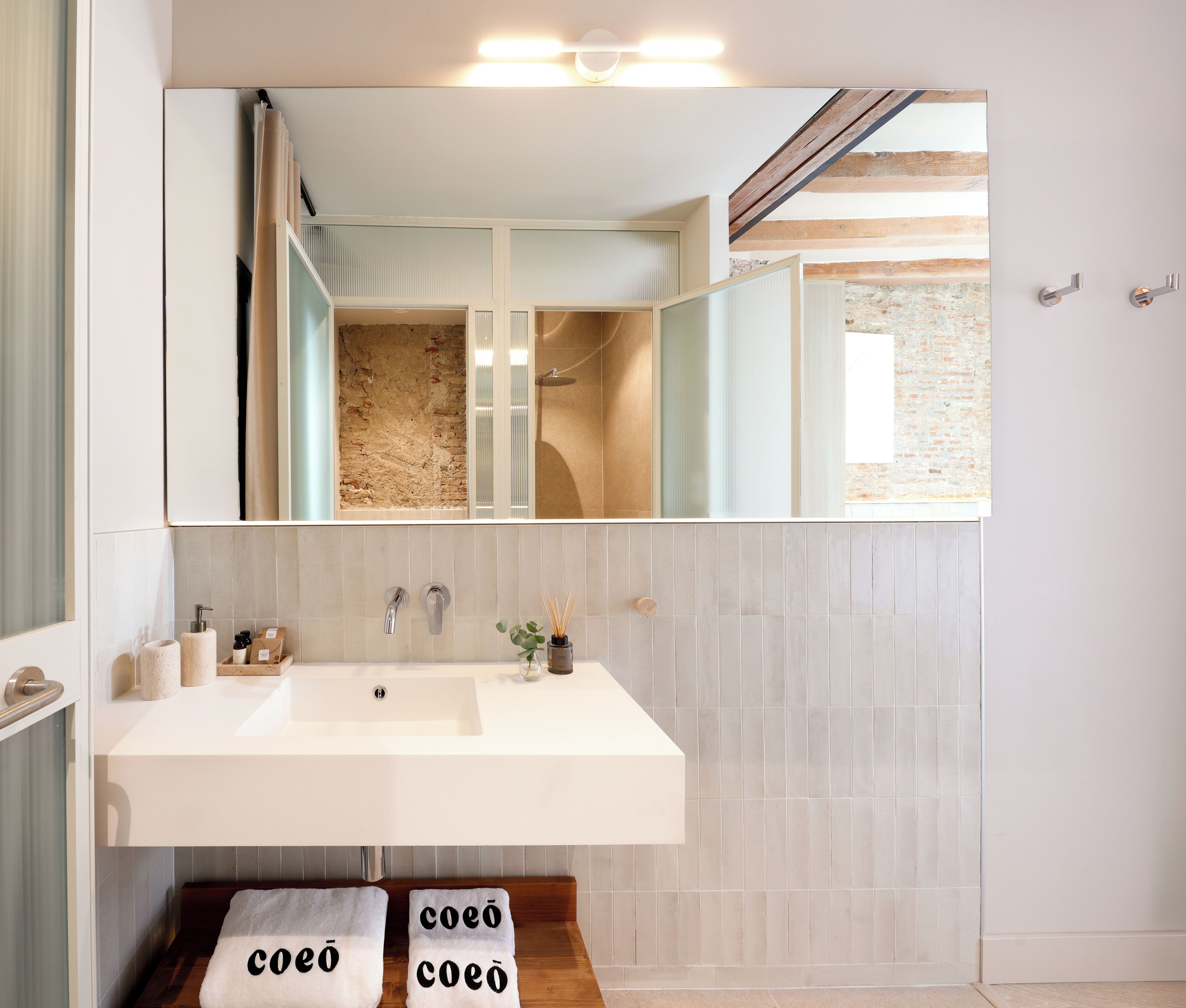 A bathroom with a large mirror, a white sink, and two towels with the word "coeo" on them.