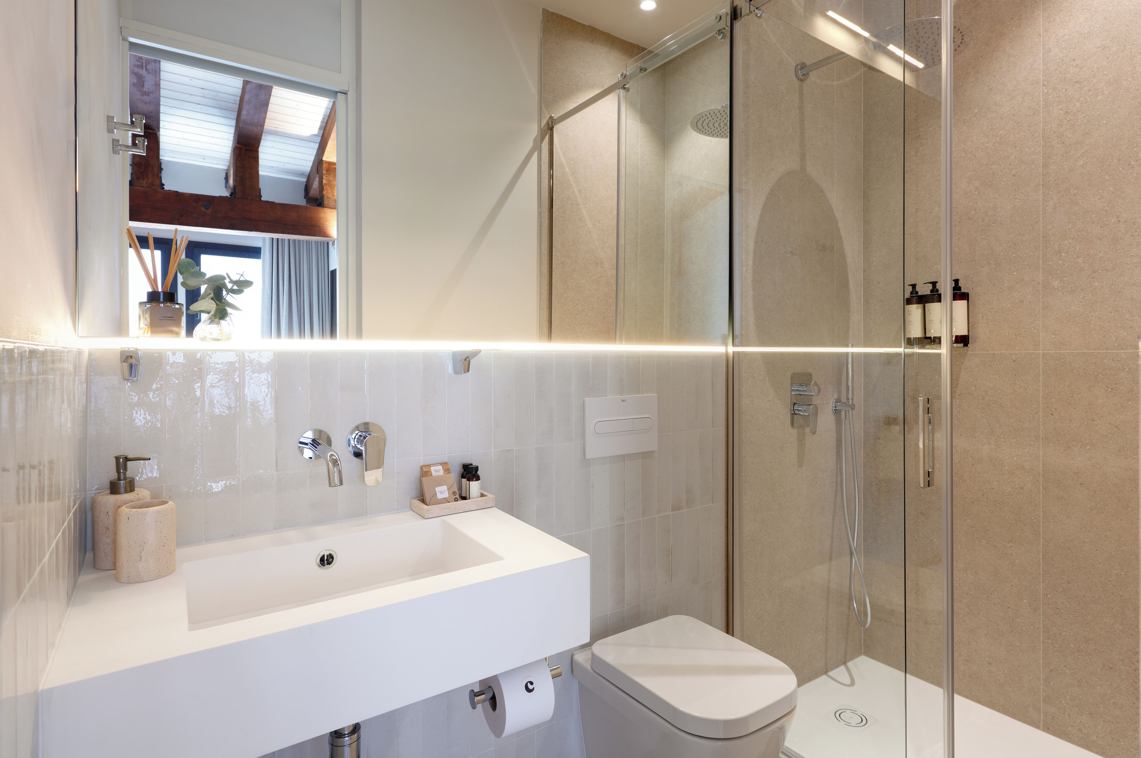 Un baño moderno con ducha envuelta en vidrio, un lavamanos blanco y un inodoro.