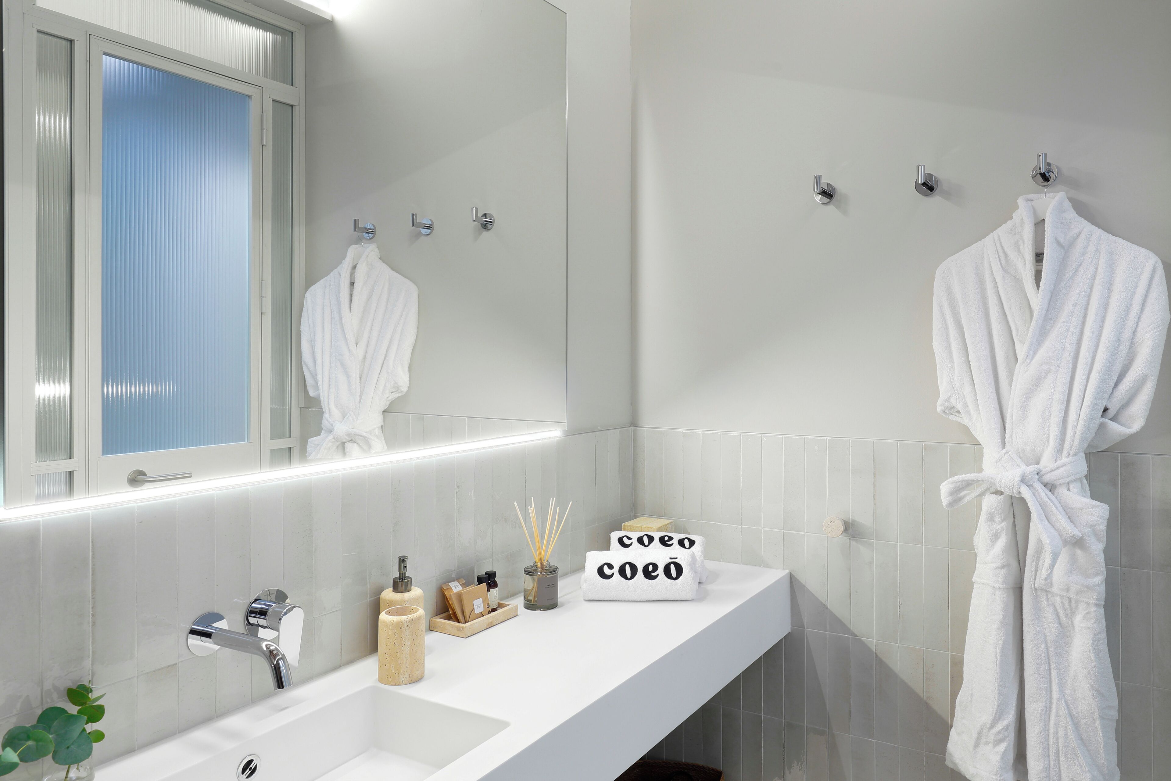 Une salle de bain moderne avec un grand miroir, un lavabo blanc et un peignoir accroché au mur.